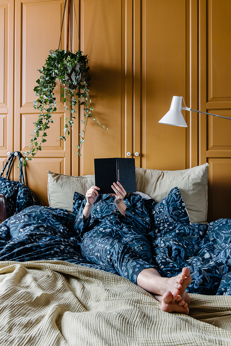 En person ligger och läser i sängkläder med mönster skapat av Plingsulli för House of Rym